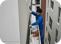 WWorker cleaning gutters on a commercial building in Oceanside, CA