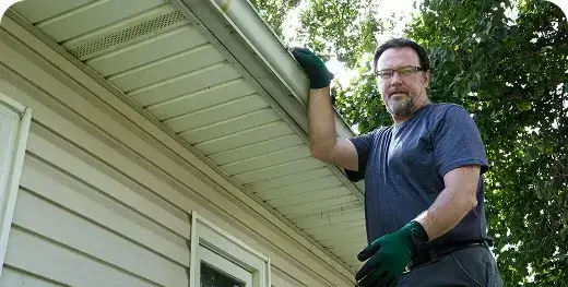 Homeowner cleaning roof gutters from a ladder in Oceanside, CA