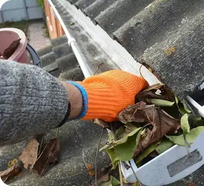 Pro pulling packed leaves out of a roofline gutter by hand in Oceanside, CA