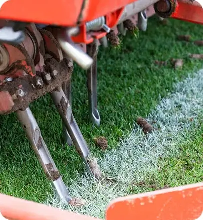 Landscaper operating a core aerator leaving soil plugs across a front lawn in Portland, ME