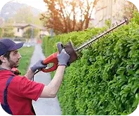 Crew member finishing hedge edges with hand shears near a front porch in Logan, UT